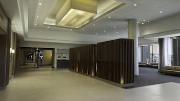 A modern hotel lobby with a high ceiling, recessed lighting, a seating area with a sofa and armchairs, and a reception desk.