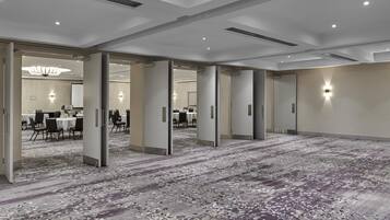 A spacious hotel lobby with a carpeted floor, multiple doors leading to conference rooms, and a chandelier.