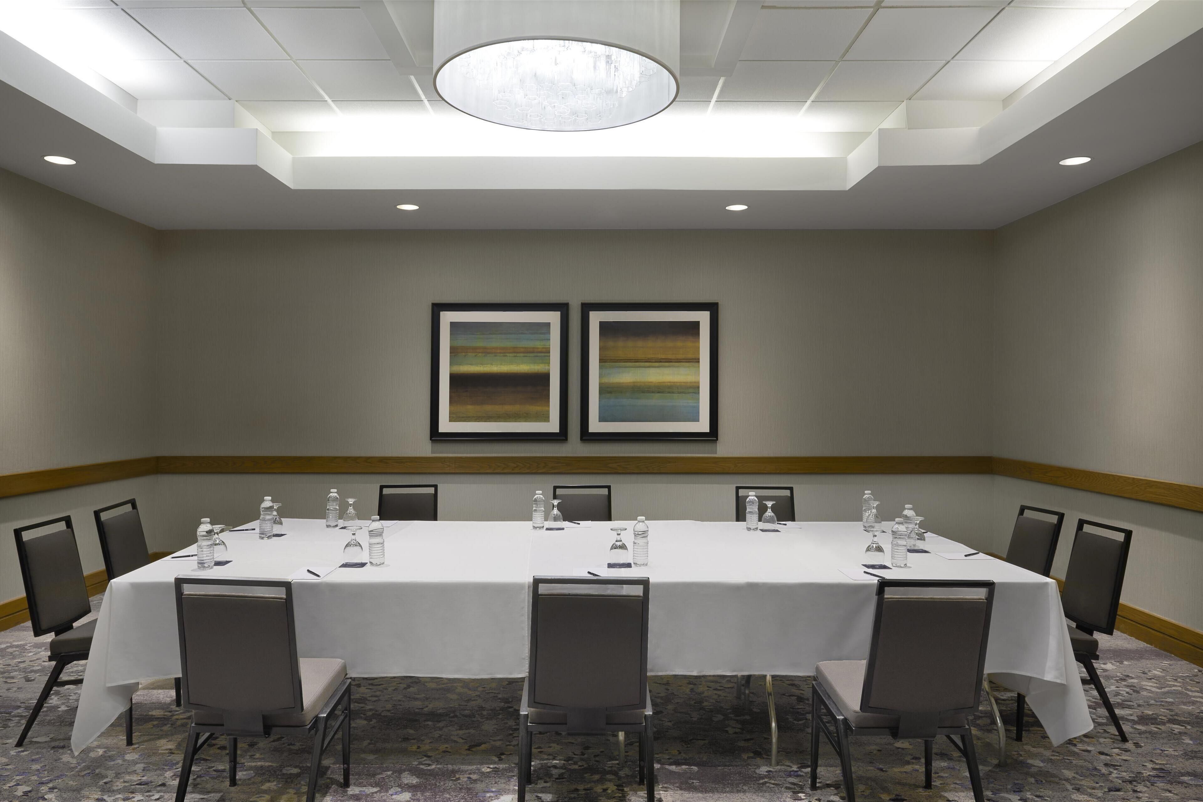 A conference room with a long table, chairs, and framed artwork on the wall.