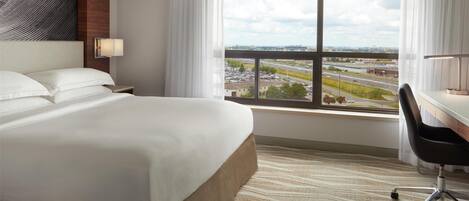 A hotel room with a large bed, a desk, and a view of a highway and buildings.