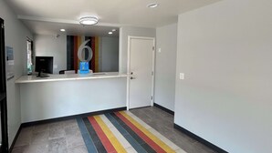 A hallway with a reception desk, a security camera, and a door. - Motel 6 Lake Elsinore, CA (Lake Elsinore)