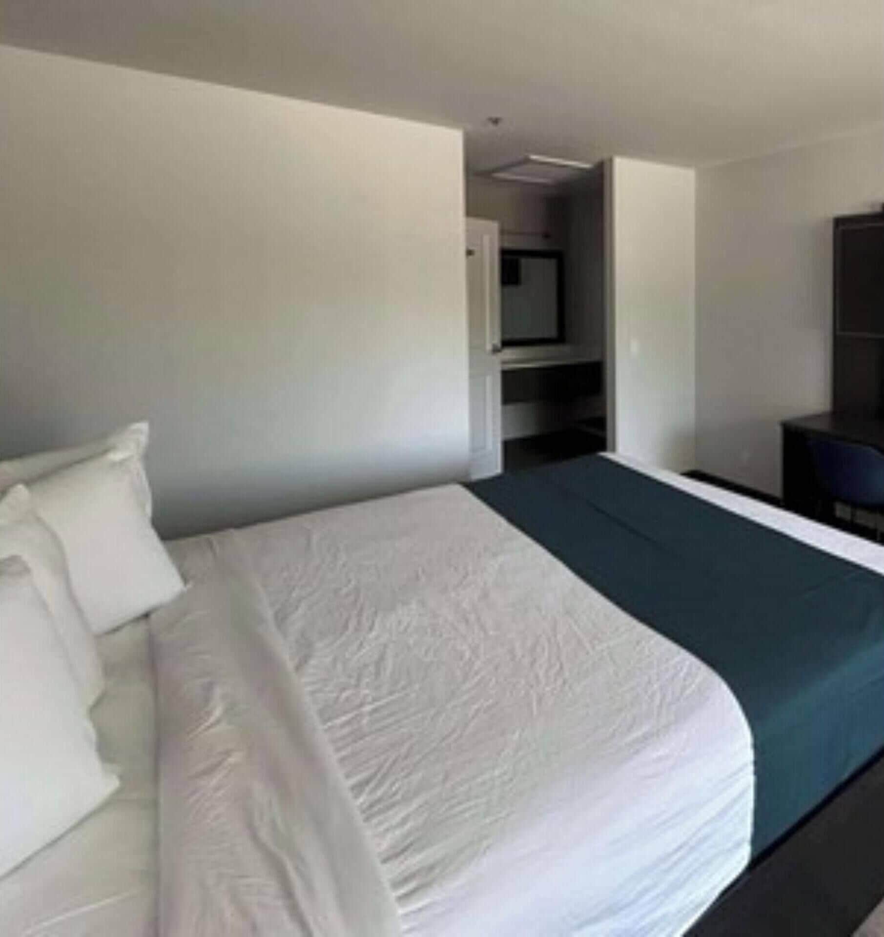 A hotel room with a large bed, a desk, and a wardrobe.