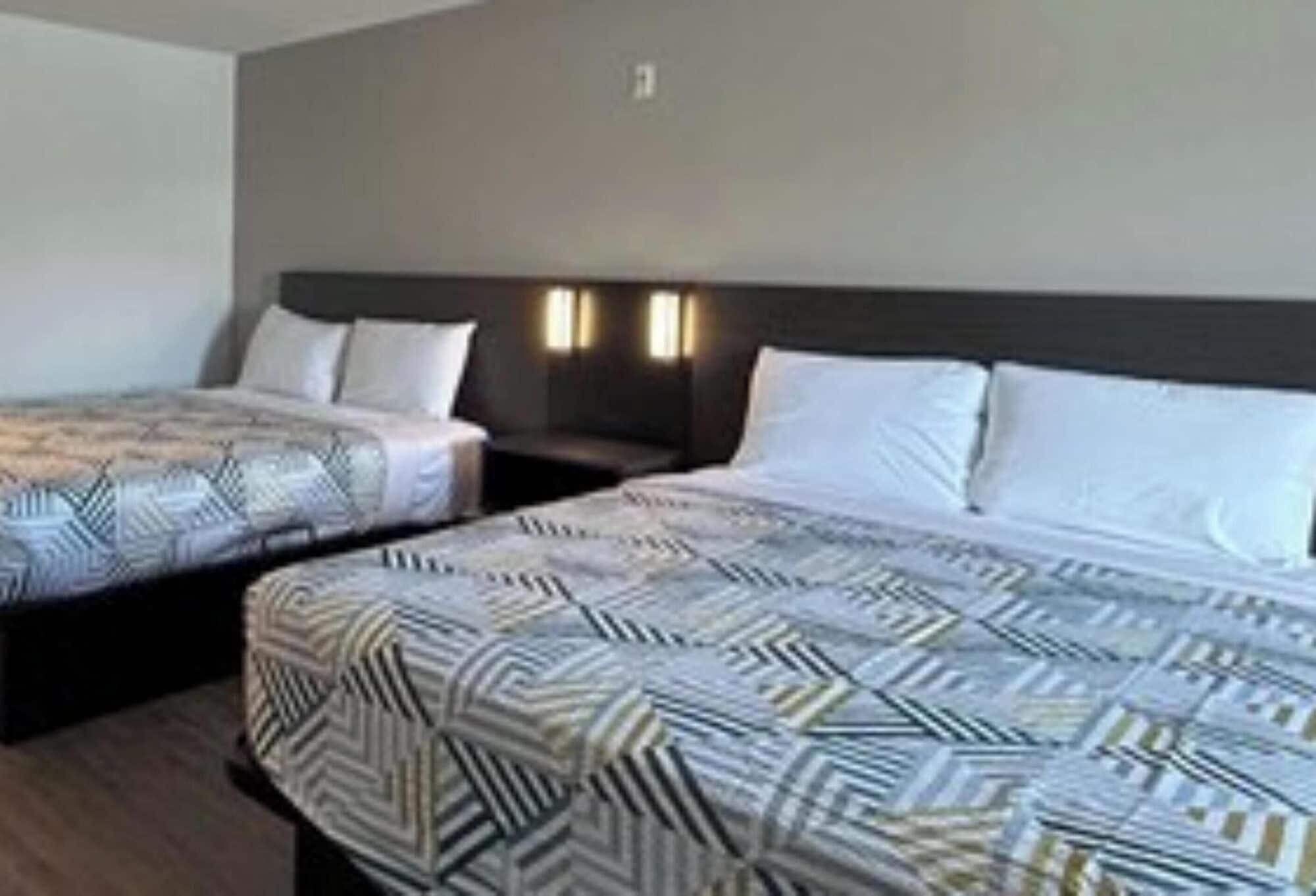 A hotel room with two beds, each with patterned bedding and a dark headboard.
