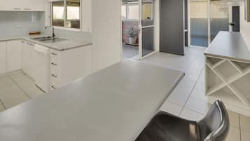 A modern kitchen with white cabinetry, a stainless steel sink, and a dining area with a table and chairs.