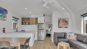 A modern kitchen with a central island, a dining area with a table and chairs, a grey sofa with cushions, and a small wooden stool. - BIG4 Ingenia Holidays Queenscliff Beacon (Queenscliff)