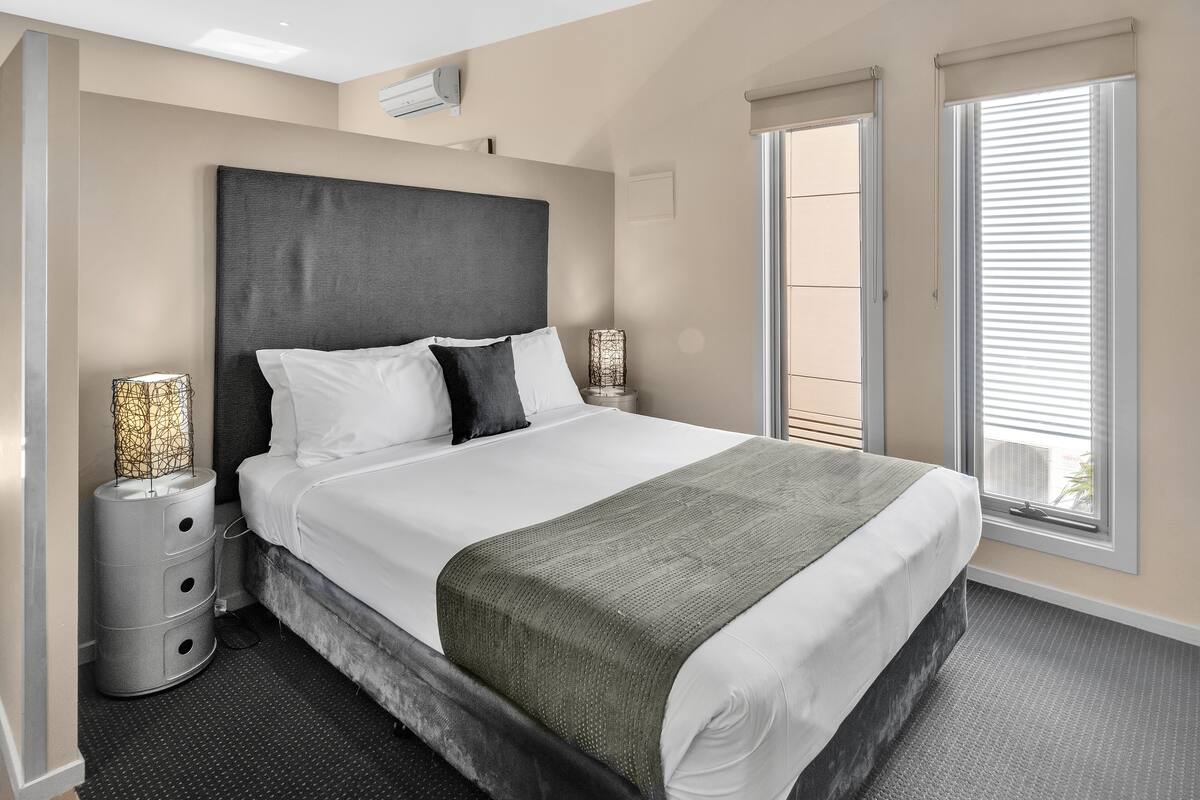 A modern bedroom with a large bed, a headboard, bedside lamps, and a view of the outside balcony.
