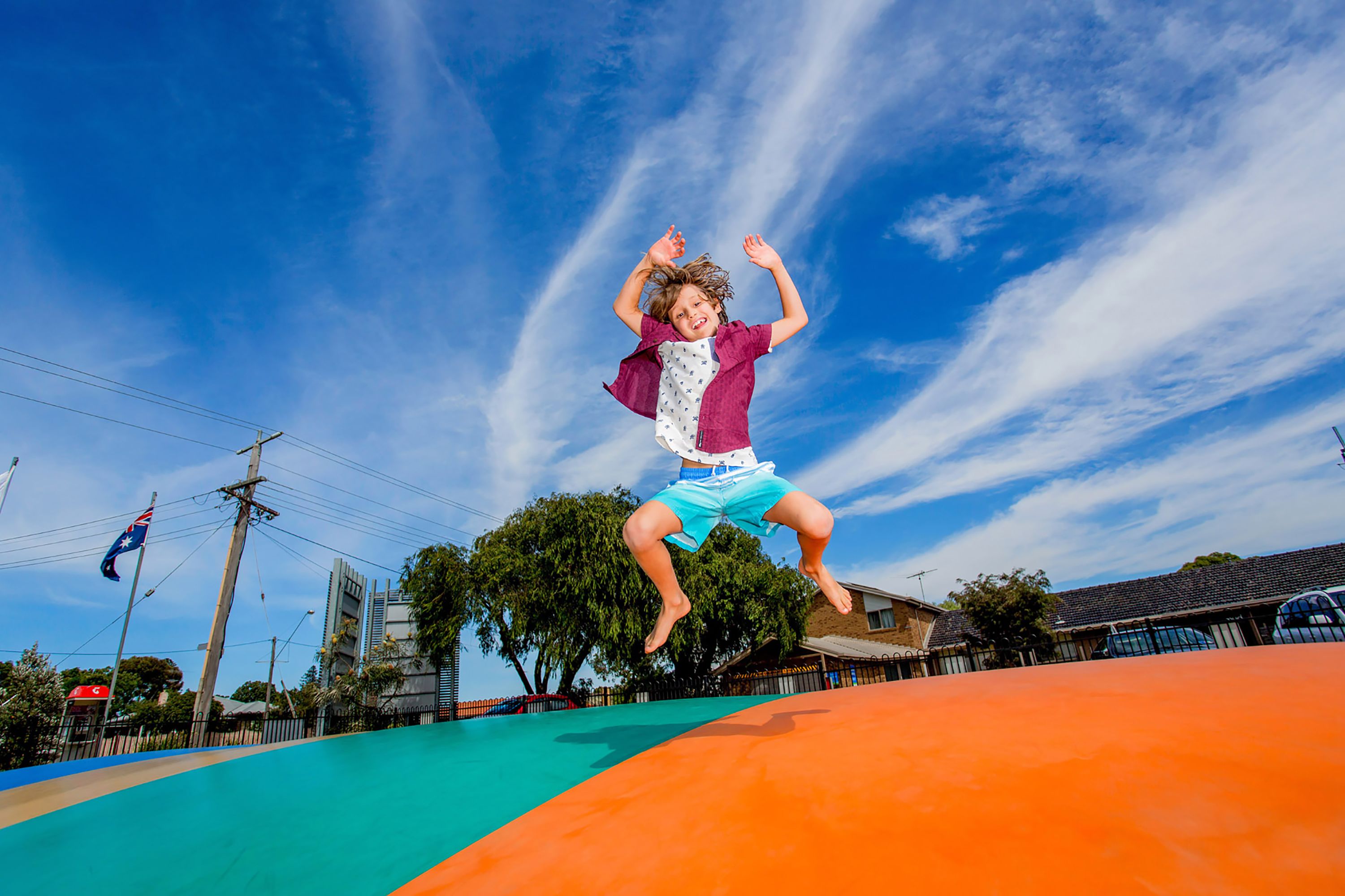 A child jumping on a trampoline with a clear blue sky and buildings in the background.
