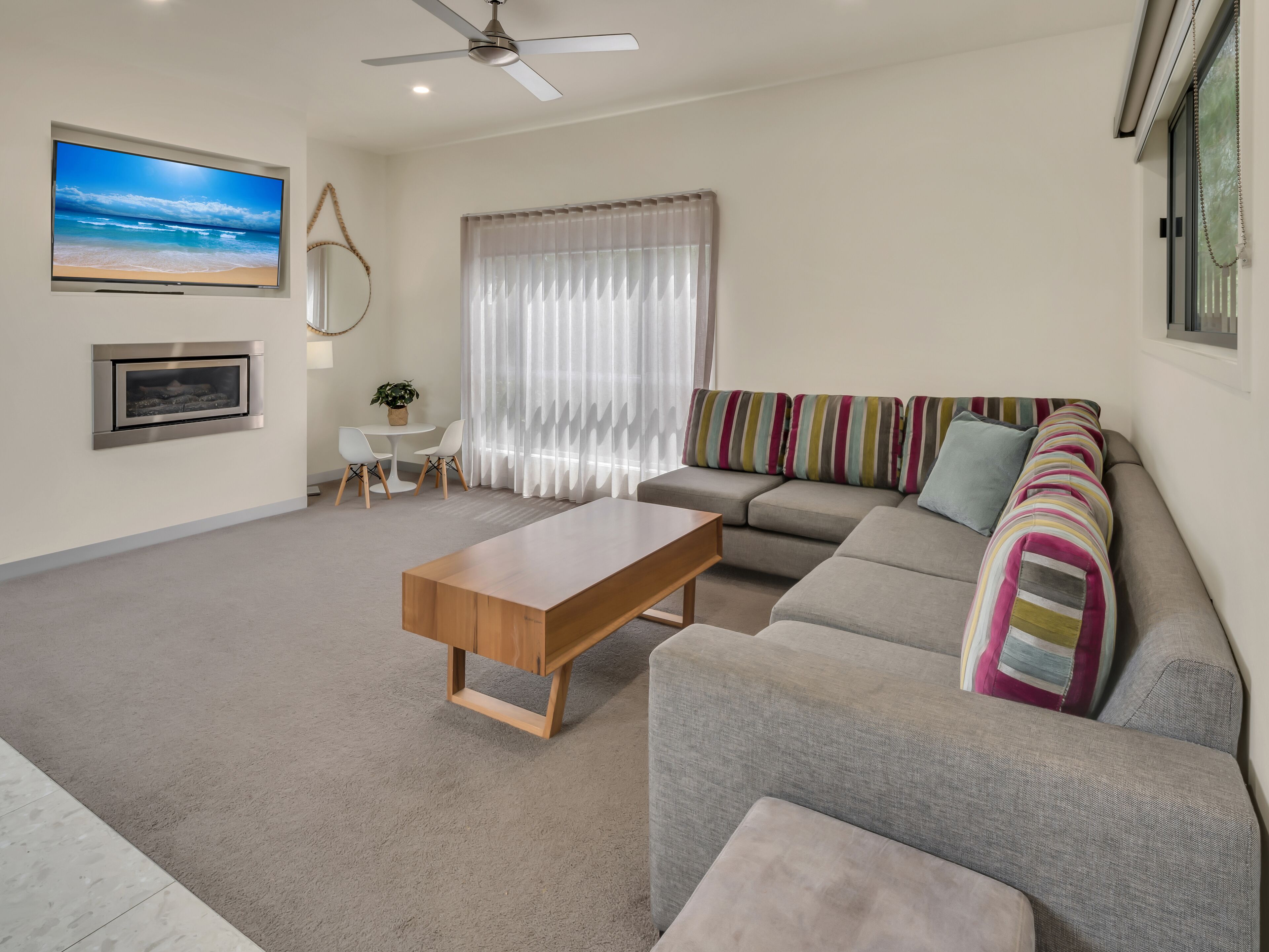 A modern living room with a sofa, a wooden coffee table, a TV mounted on the wall, and a ceiling fan.