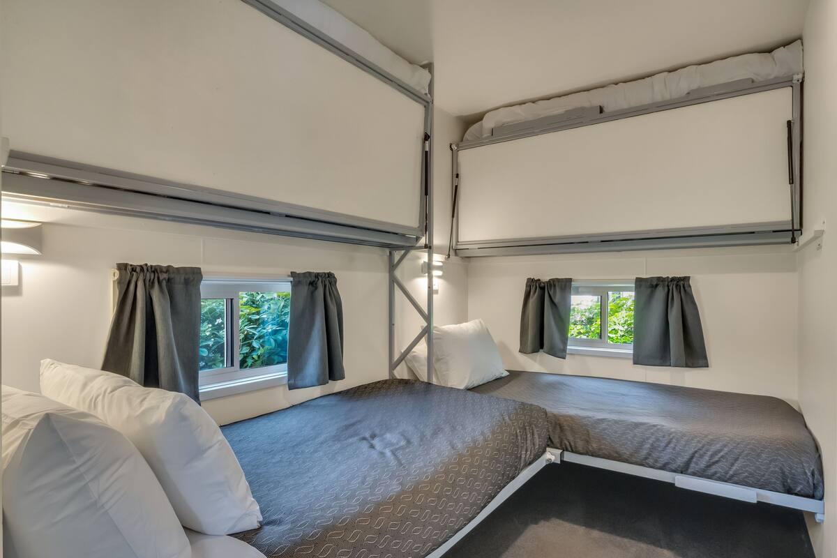 A compact room with two beds, each with a window and curtains.