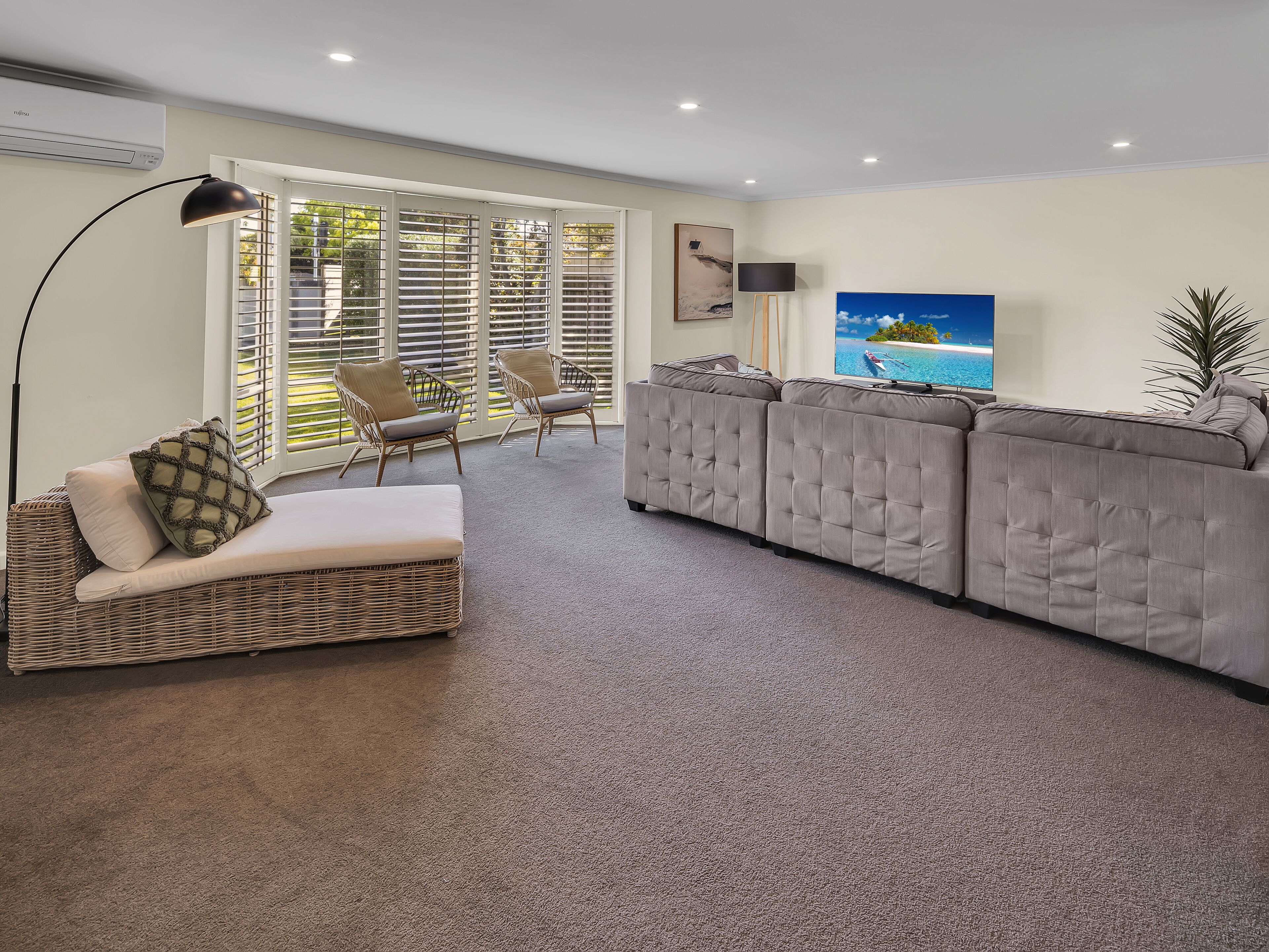 A living room with a sofa, two armchairs, a floor lamp, and a TV.