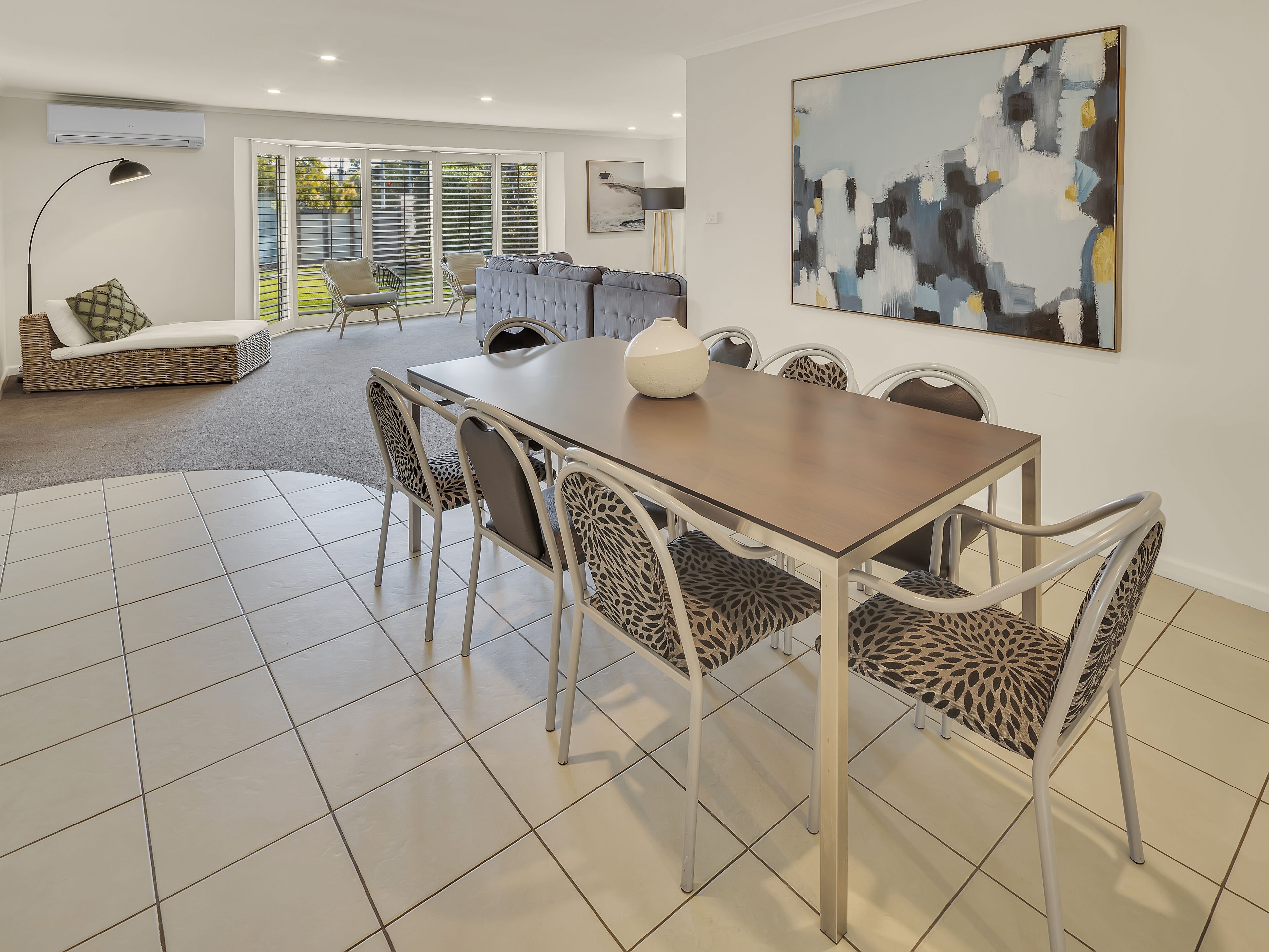 A dining area with a table and chairs, a sofa, and a large abstract painting on the wall.