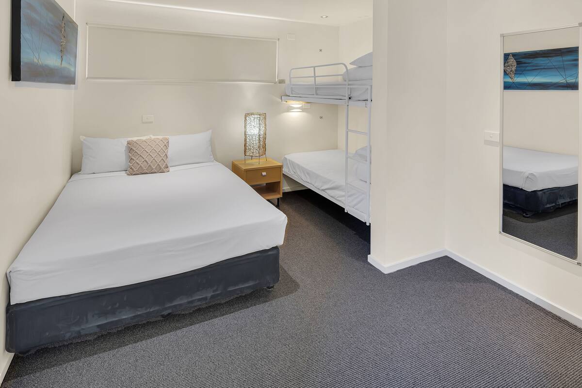 A hotel room with a large bed, a smaller bed, a nightstand, a lamp, and a mirror.