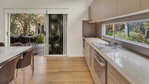 A modern kitchen with a large window, sliding glass door to a patio, and a dining area with chairs. - BIG4 Ingenia Holidays Queenscliff Beacon (Queenscliff)