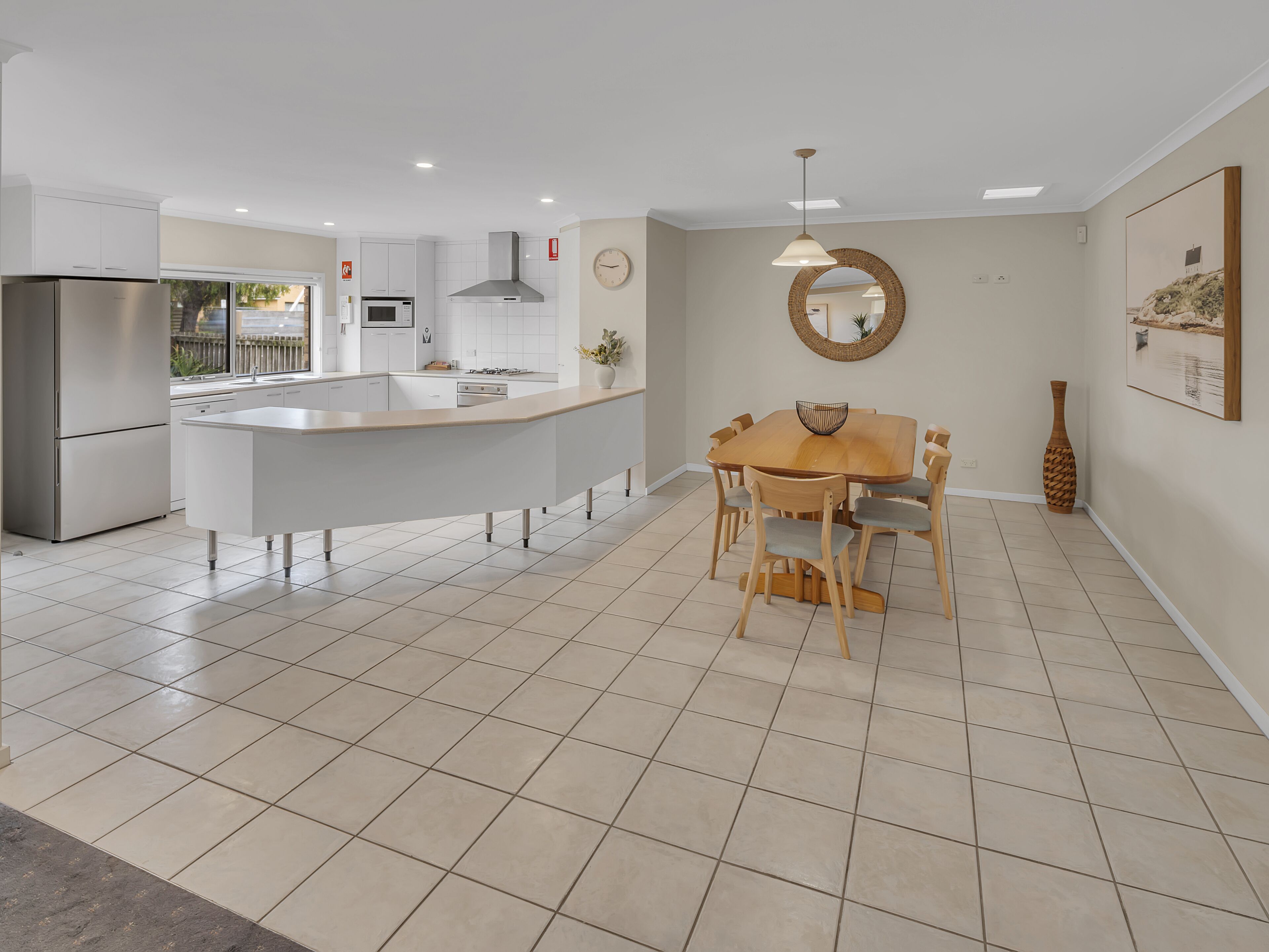A modern kitchen with a central island, a dining area with a wooden table and chairs, and a large mirror on the wall.