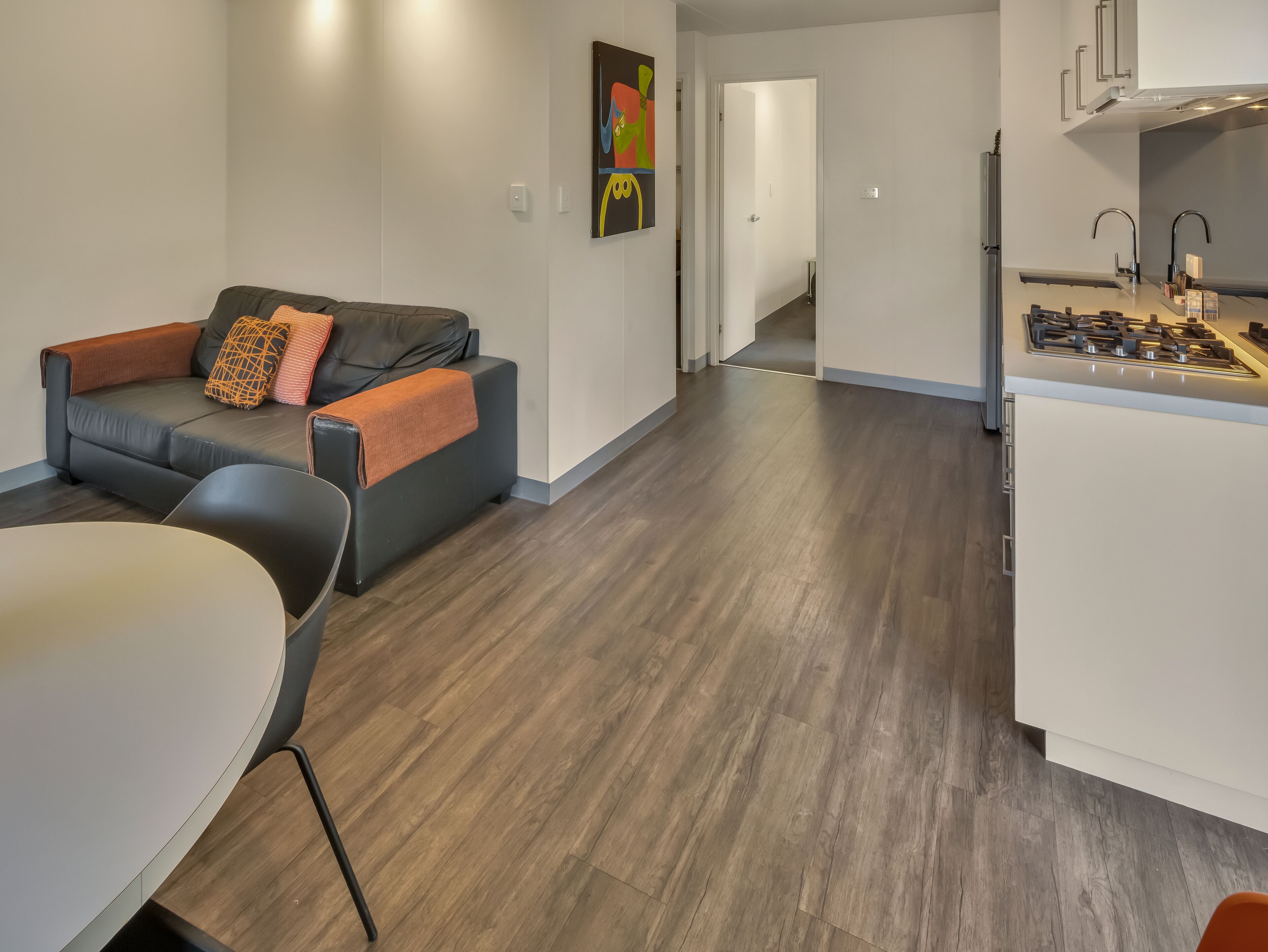 A modern living room with a grey sofa, a dining table, and a kitchen area with a stove.