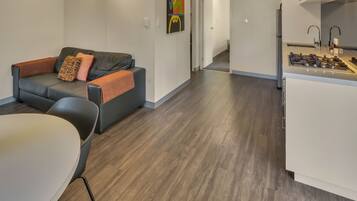 A modern living room with a grey sofa, a dining table, and a kitchen area with a stove.