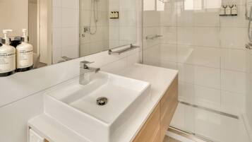 A modern bathroom with a white sink, a glass shower enclosure, and toiletries on a shelf.