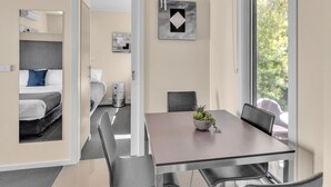 A modern hotel room with a dining area featuring a table and chairs, a small potted plant, and artwork on the walls. - BIG4 Ingenia Holidays Queenscliff Beacon (Queenscliff)