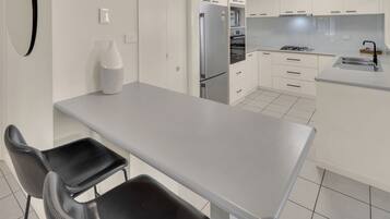 Una cocina moderna con armarios blancos, un refrigerador de acero inoxidable, una estufa a gas y una zona de comedor con una mesa y dos sillas.