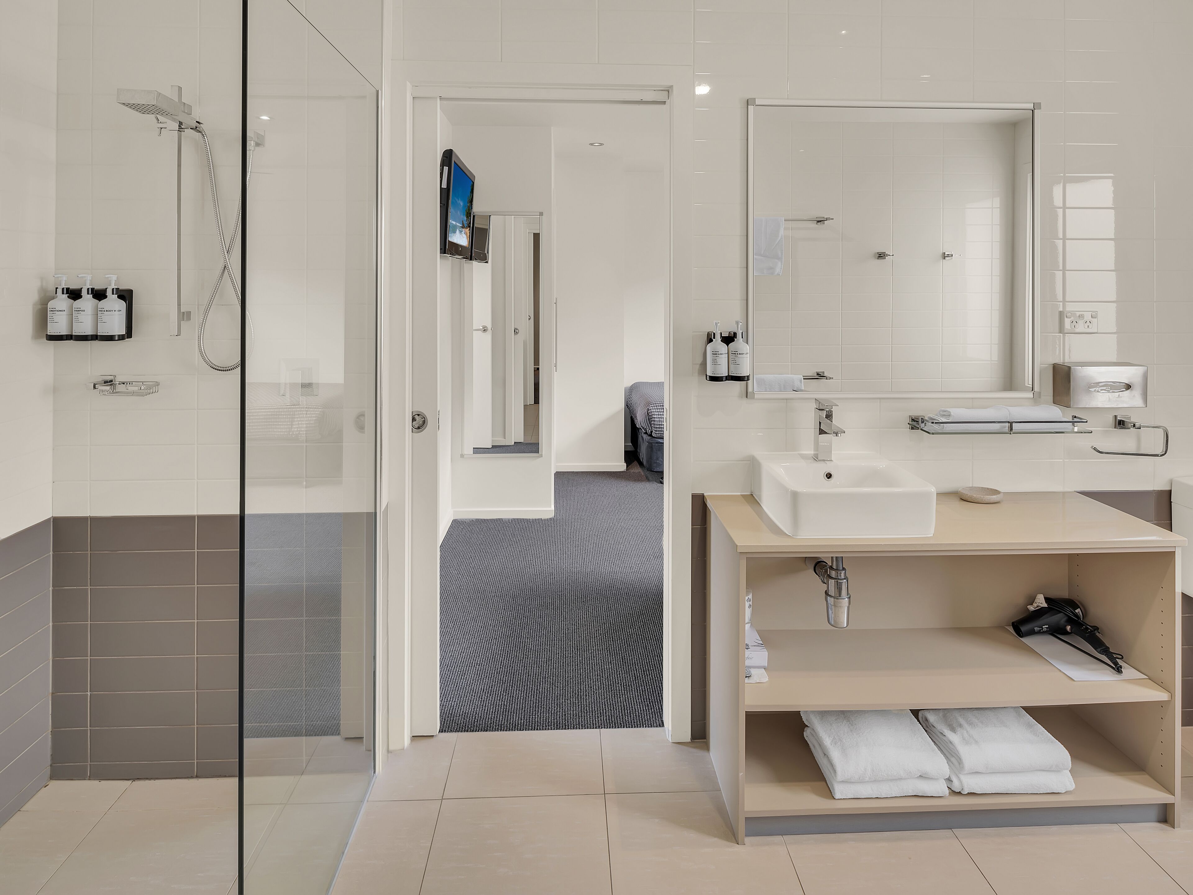 Une salle de bain moderne avec une douche à parois de verre, un grand miroir et un meuble-lavabo doté d’un évier et d’un porte-serviettes.