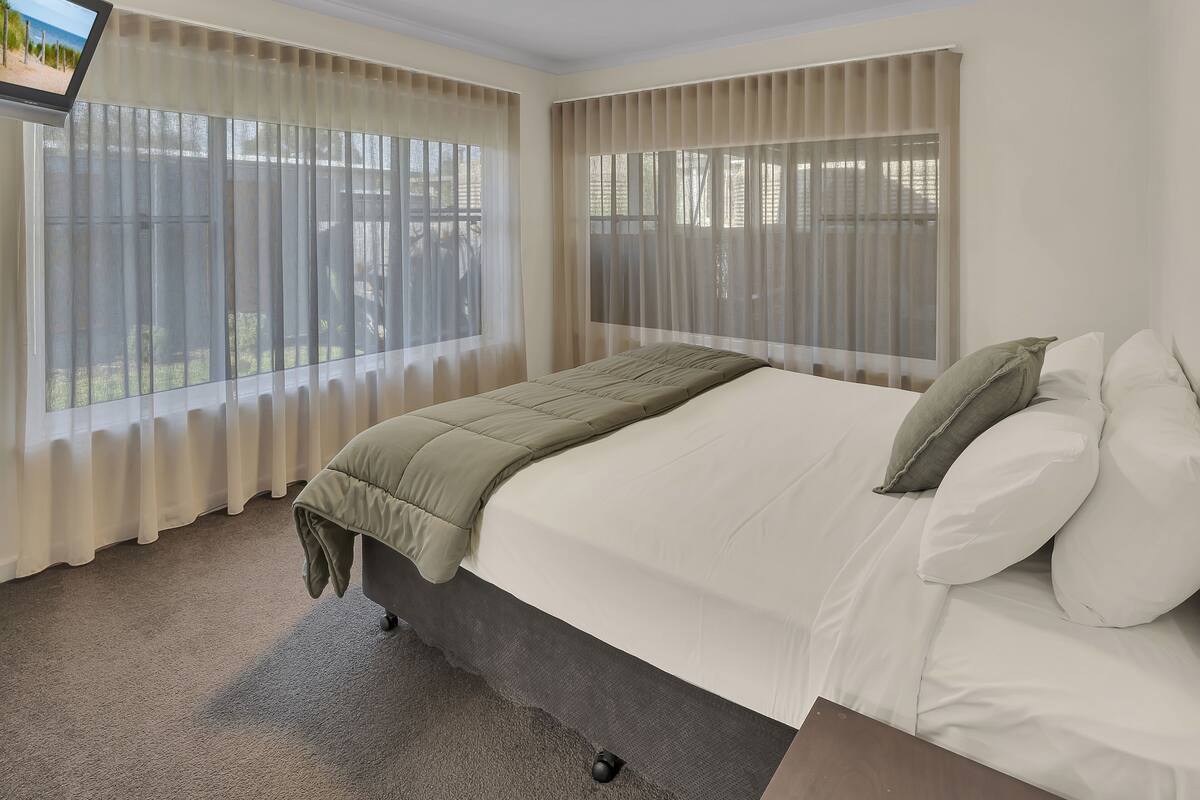 A bedroom with a bed, curtains, a TV, and a view of the outdoors.
