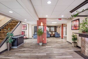 Un vestíbulo de hotel con mostrador de recepción, escalera, zona de estar y plantas en macetas.