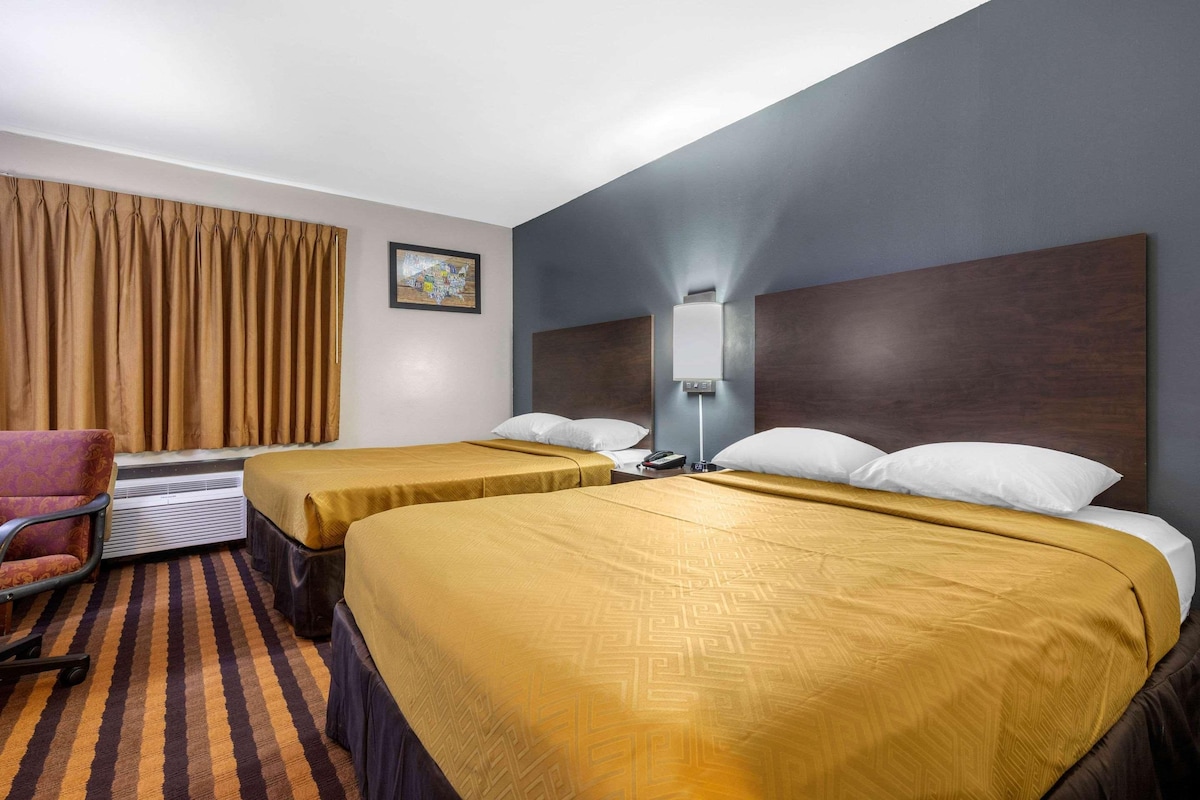 A hotel room with two beds, a desk, a chair, and a large window with curtains.