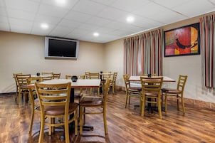 Un salón de conferencias con mesas y sillas de madera, un televisor de pantalla plana y un cuadro abstracto colorido en la pared.