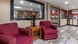 A waiting area with red upholstered chairs, a wooden table with a vase of flowers, and a large window. - Econo Lodge Milwaukee Airport (Milwaukee)