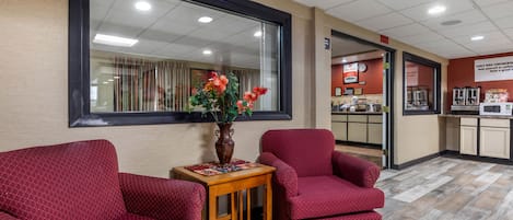 Un área de espera con sillones tapizados en rojo, una mesa de madera con un jarrón de flores y un ventanal grande.