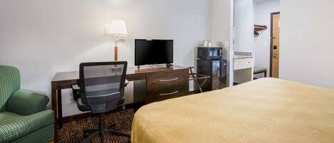A hotel room with a bed, a desk with a computer and a television, a microwave, and a green armchair.