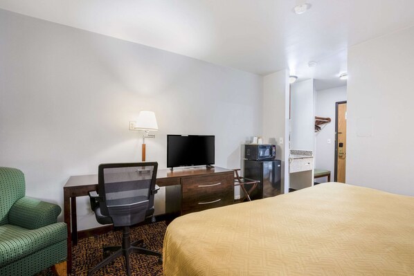 Habitación de hotel con cama, escritorio con computadora y televisor, microondas y un sillón verde.