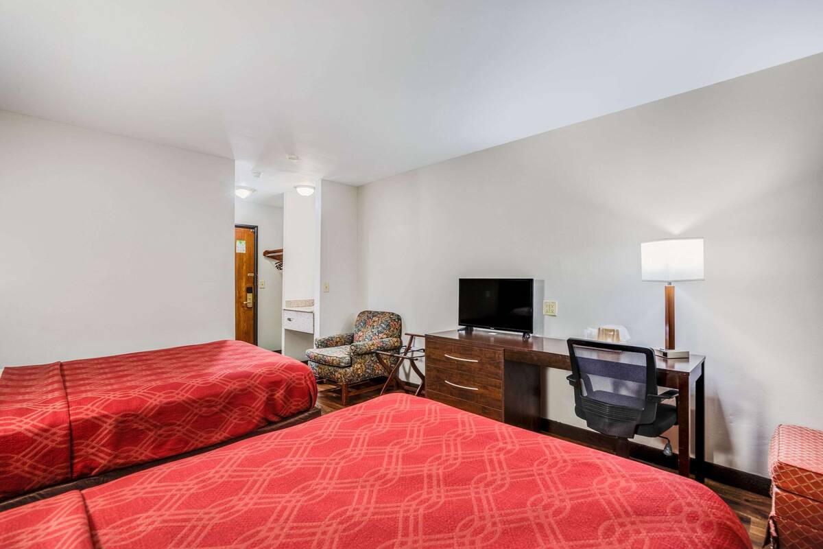 Una habitación de hotel con dos camas, un escritorio, una silla, un televisor y una lámpara.