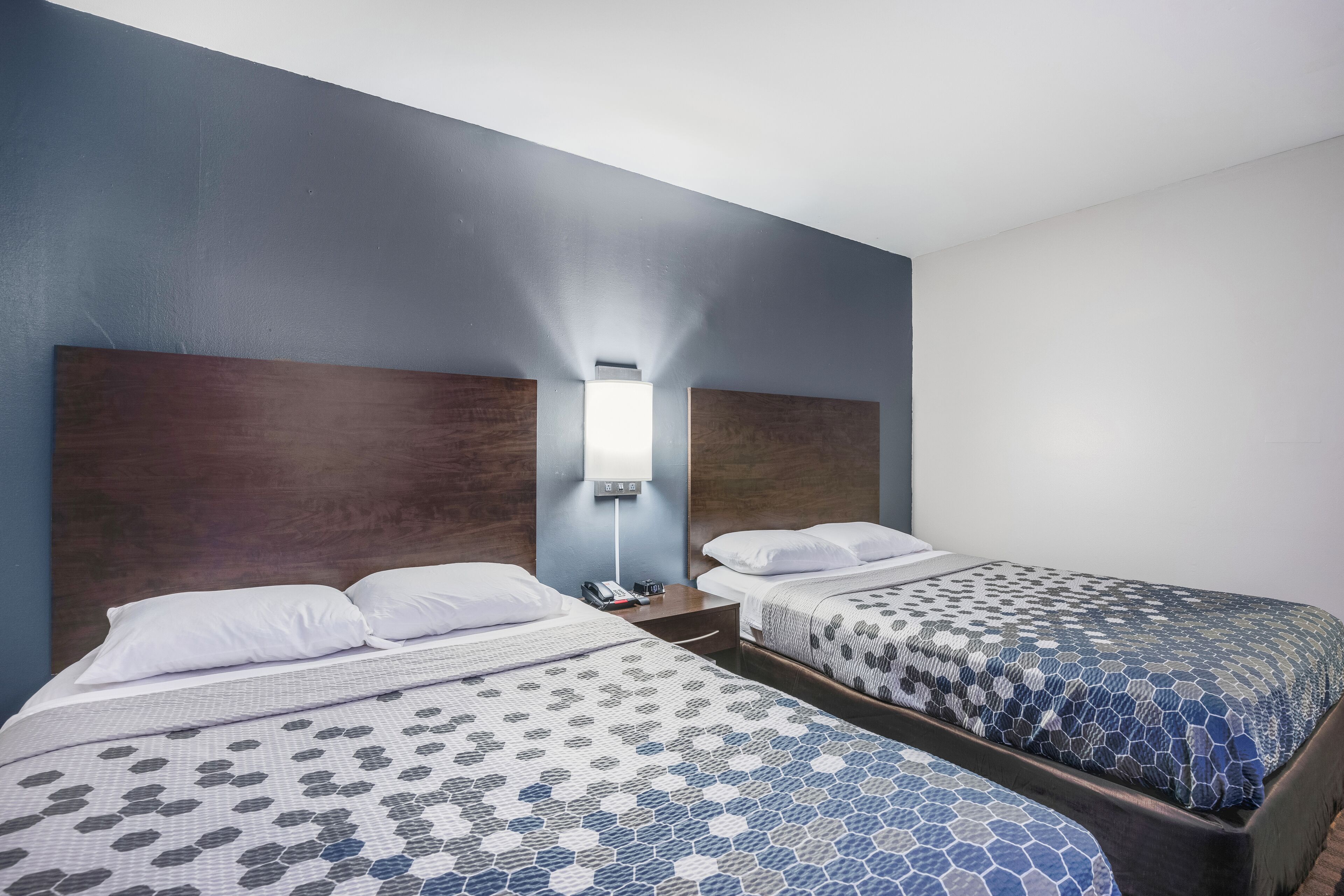 Una habitación de hotel con dos camas, una mesita de noche y una lámpara fijada a la pared.