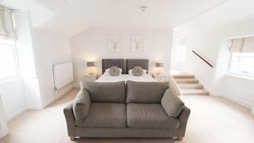 A bedroom with a large gray sofa, a bed with two decorative pillows, and a staircase leading to an upper floor.