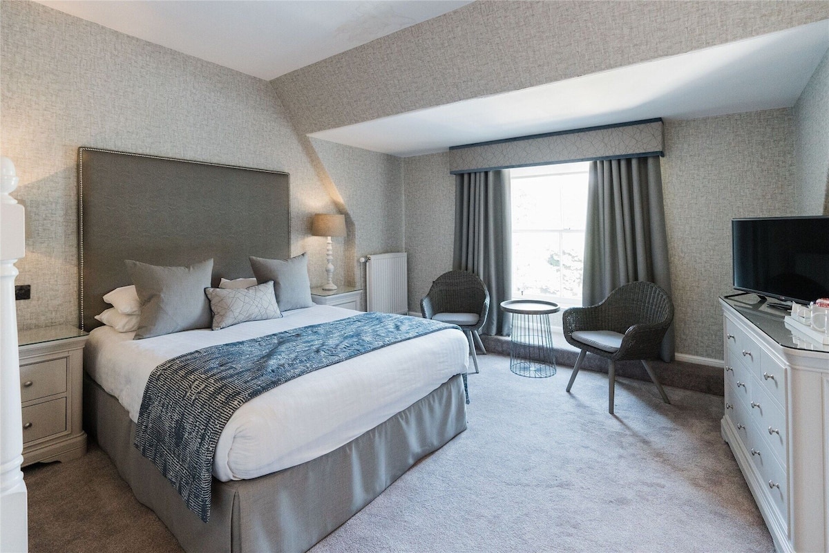 A hotel room with a large bed, a TV, a chair, a small table, and a dresser.