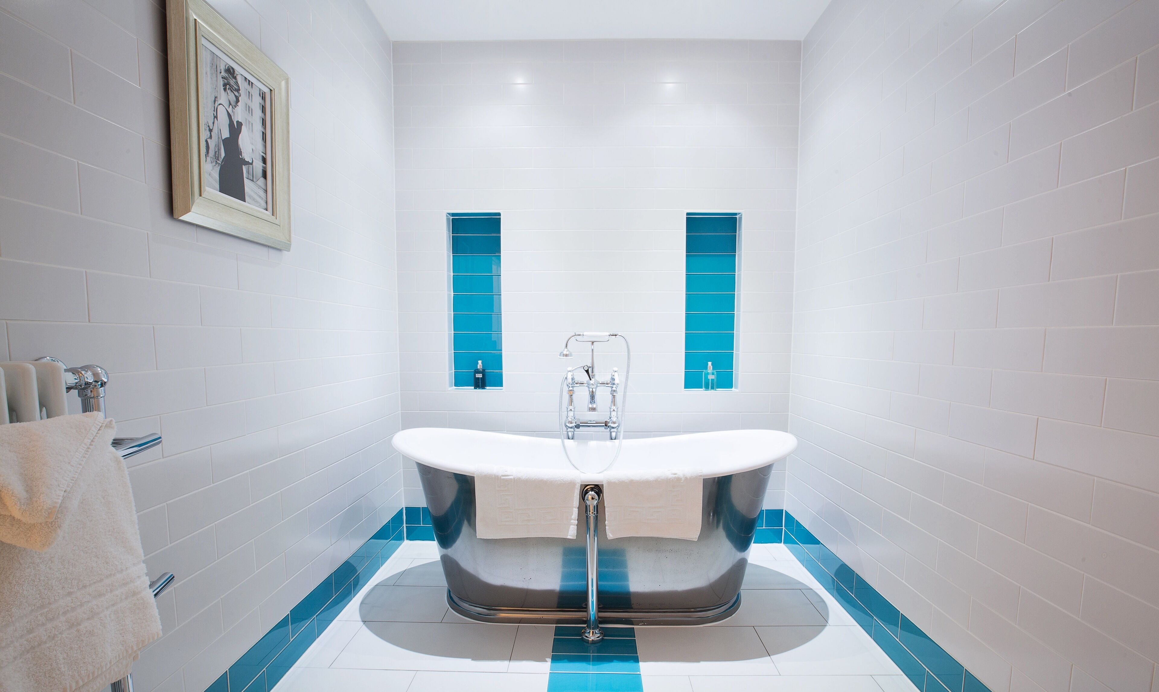 A modern bathroom with a freestanding bathtub, white tiled walls, and blue accent tiles.