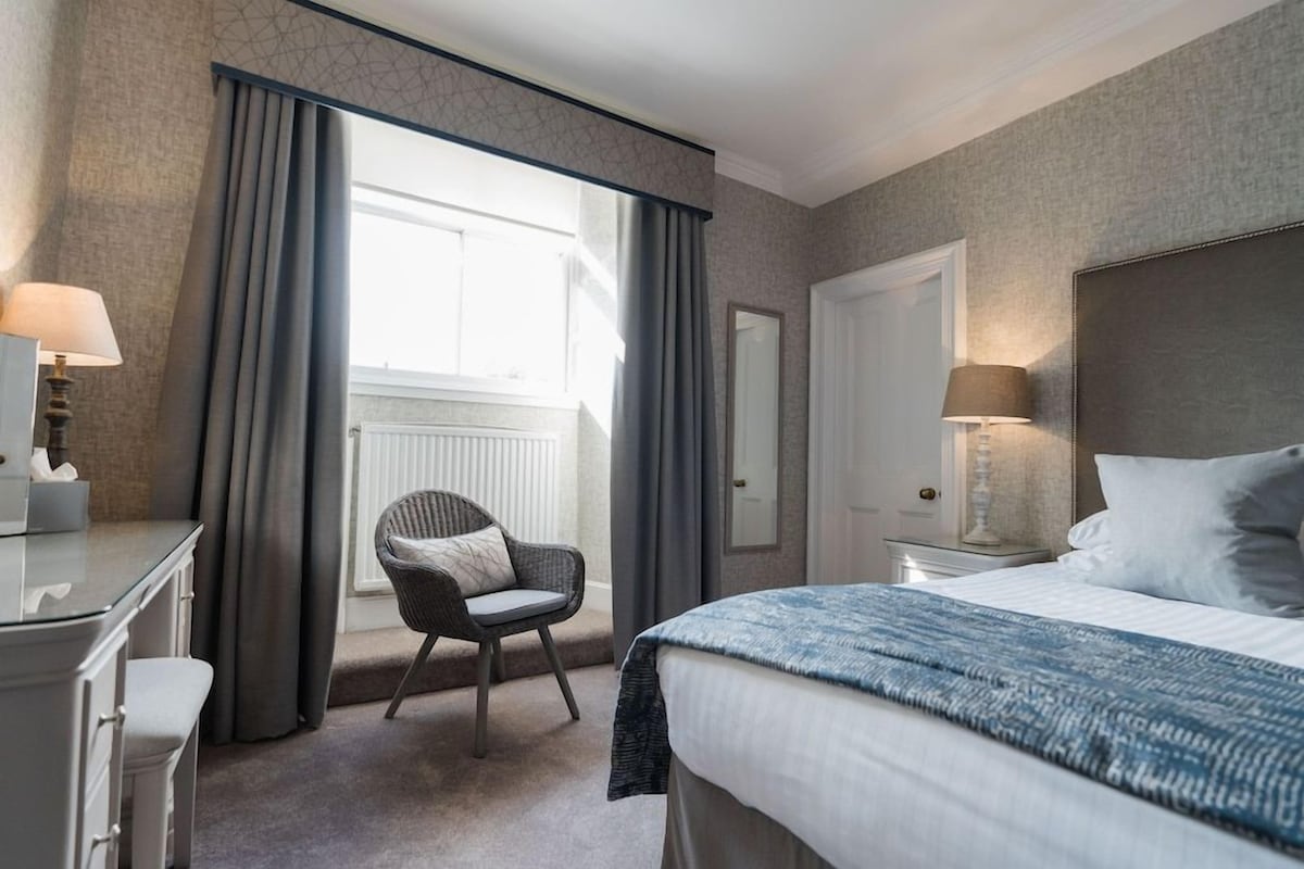 A hotel room with a large bed, a chair, a desk, and a window with curtains.