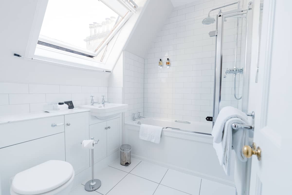 A modern bathroom with a skylight, white tiles, a bathtub, and a toilet.