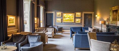 A hotel lobby with a central seating area, framed artwork on the walls, and a fireplace.