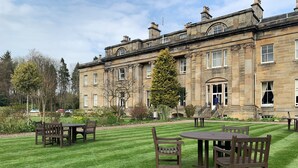 A historic stone building with a well-maintained lawn and outdoor seating area. - Balbirnie House (Glenrothes)