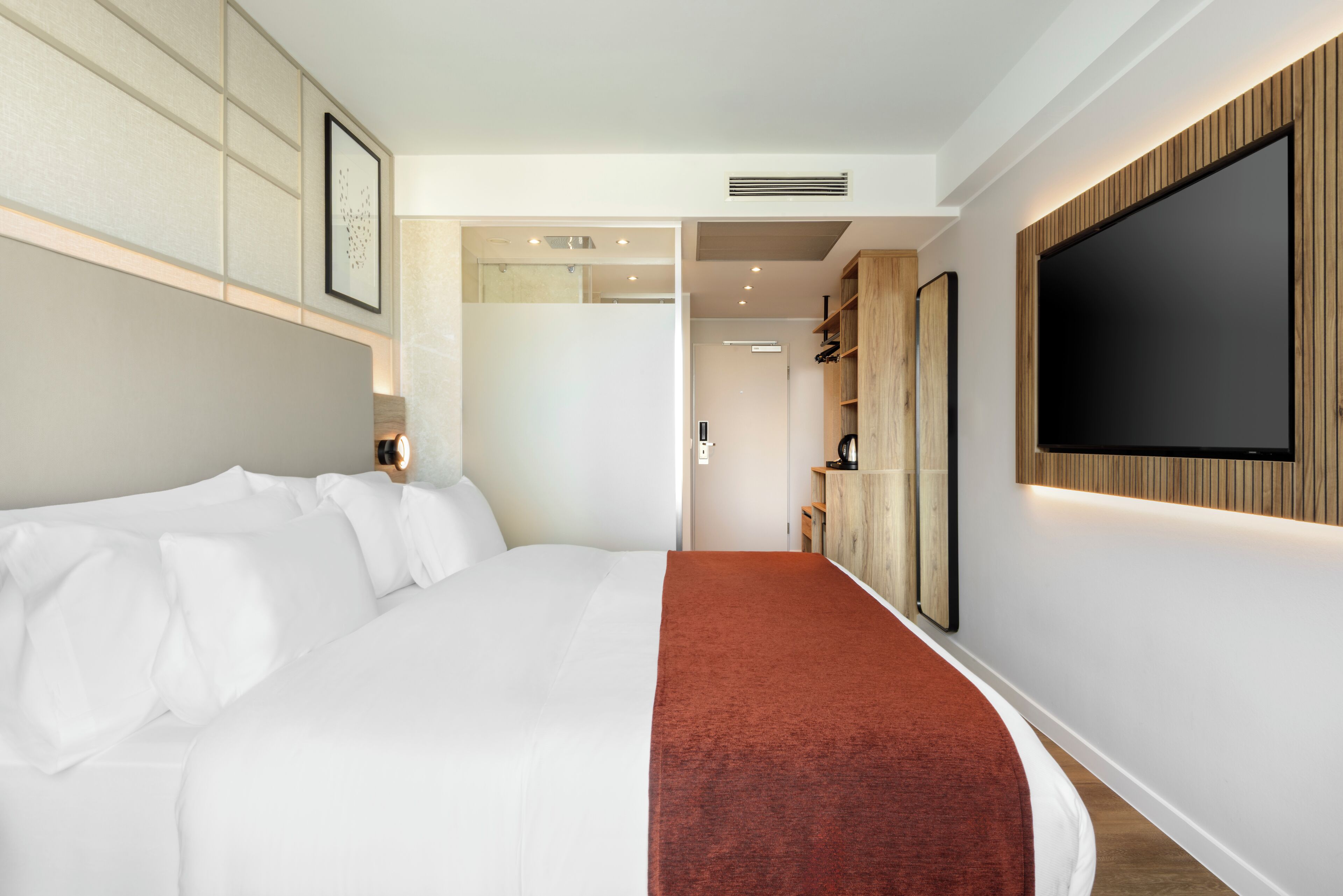 A hotel room with a large bed, a flat-screen TV mounted on the wall, a wooden cabinet, and a framed picture on the wall.