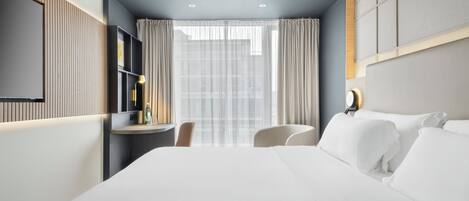 A hotel room with a large bed, a desk with a chair, a TV, and a window with curtains.