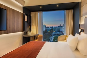 Habitación de hotel con una cama grande, un escritorio, una silla y vistas a la ciudad.