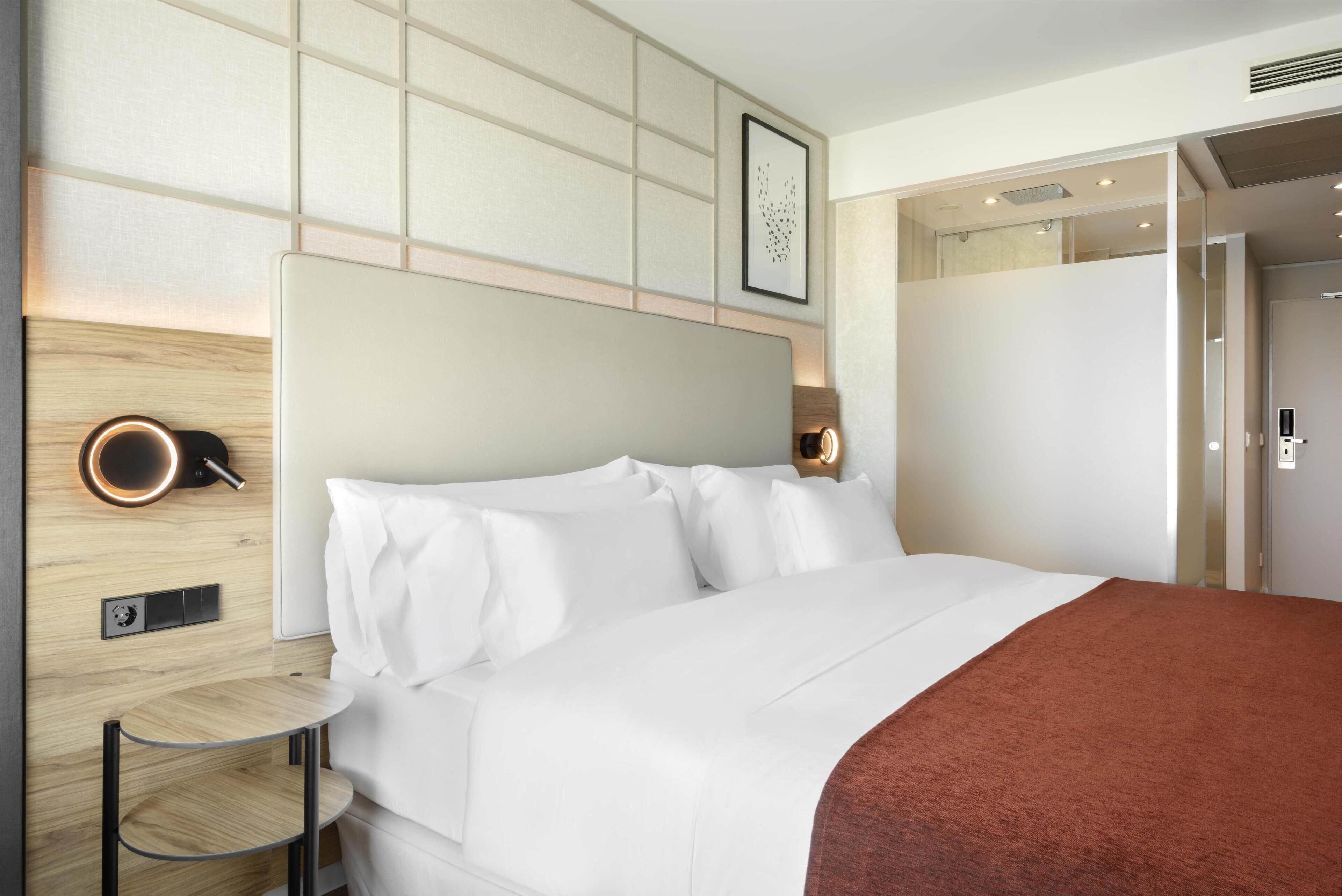 Een moderne hotelkamer met een groot bed, een klein rond tafeltje, een wandlamp en een ingelijst kunstwerk.