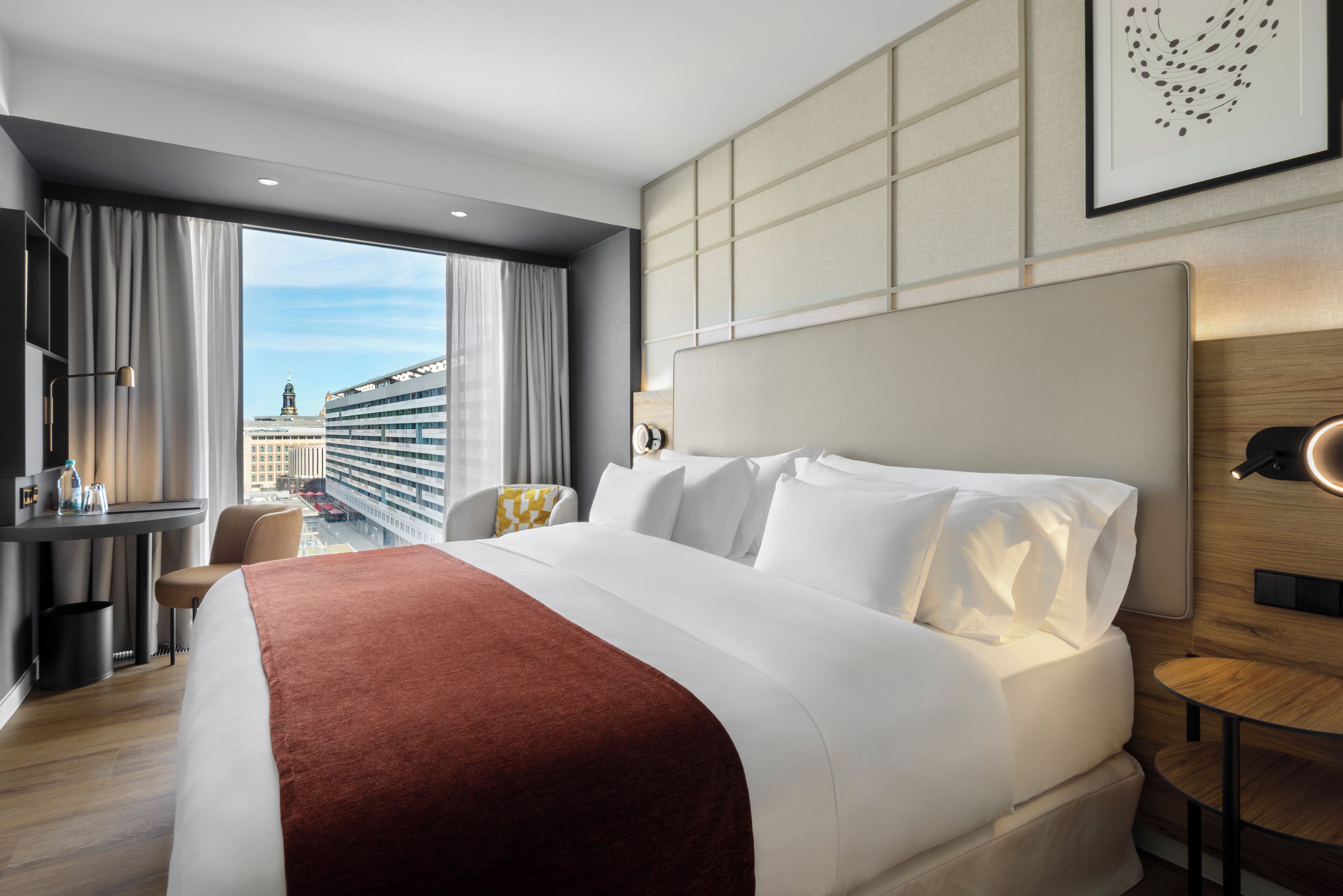 Una habitación de hotel con una cama grande, un escritorio, una silla y vistas a edificios.
