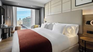 Una habitación de hotel con una cama grande, un escritorio, una silla y vistas a edificios.