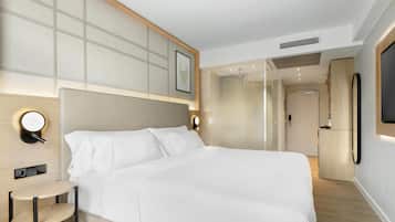 Ein modernes Hotelzimmer mit einem großen Bett, Nachttisch, wandmontiertem Fernseher und einem durch eine Glaswand abgetrennten Badezimmer.