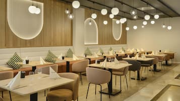 Ein modernes Restaurant mit mehreren Esstischen, Stühlen und Pendelleuchten.