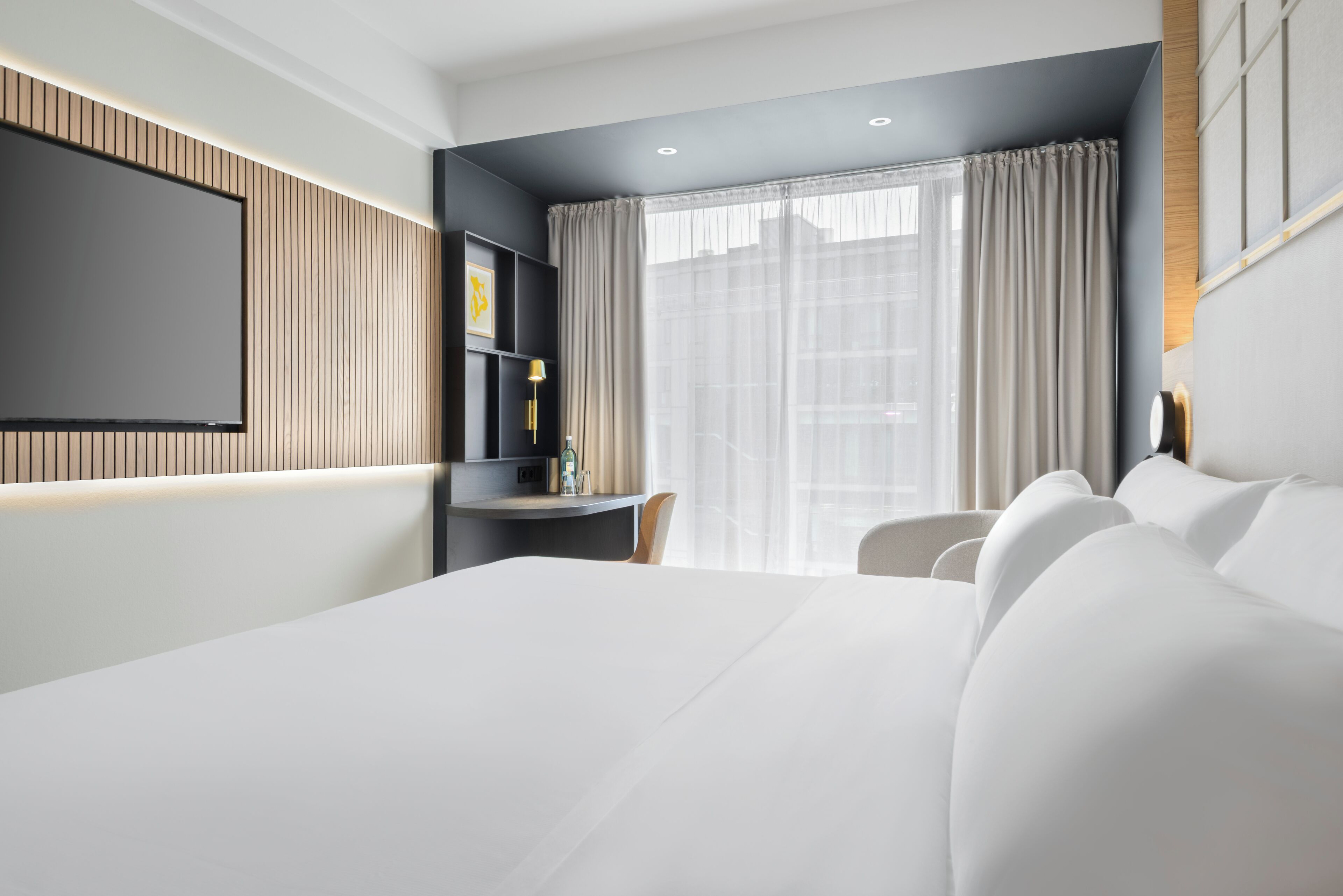 Ein modernes Hotelzimmer mit einem großen Bett, einem Schreibtisch und einem an der Wand montierten Fernseher.